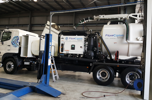 FibreComm trucks in a warehouse setting with equipment and branding by Anytime Signs