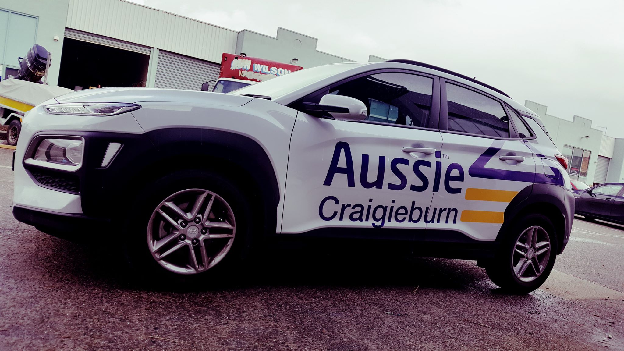 White SUV with 'Aussie Craigieburn' branding parked in front of a building. using purple and yellow vinyl decals across both sides. 