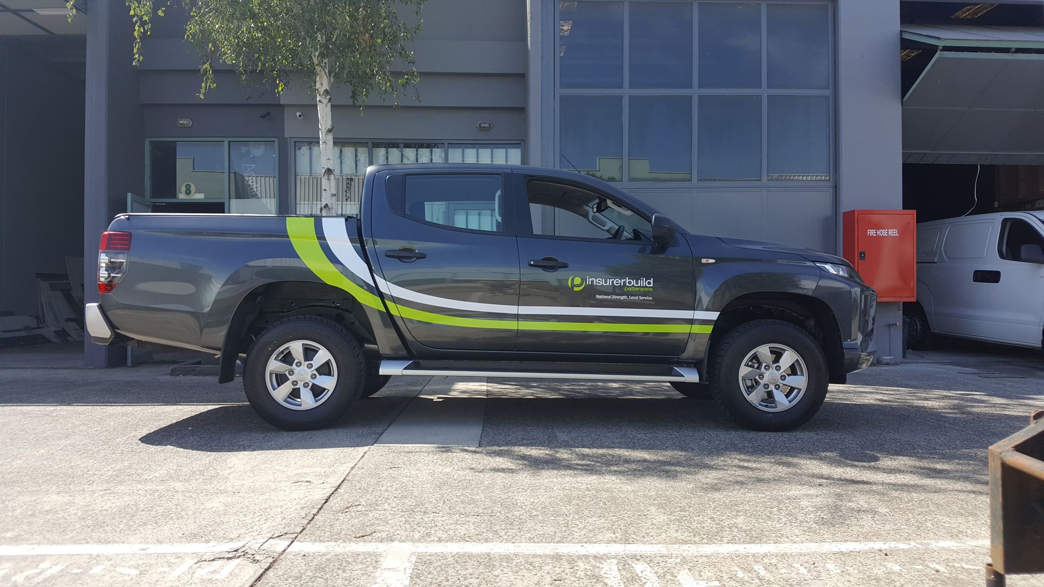 Gray pickup truck with green and black graphics parked in front of a building.