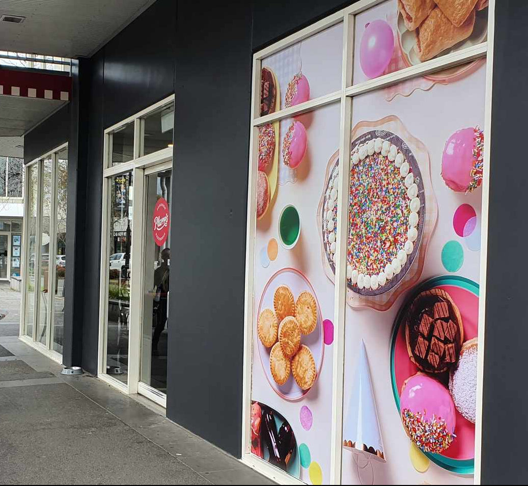 Outdoor seating area with tables and chairs outside a building with a large window display of pastries.