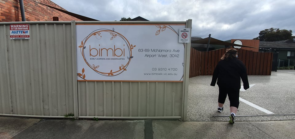 Person walking past a childcare sign on a metal gate with a cloudy sky.