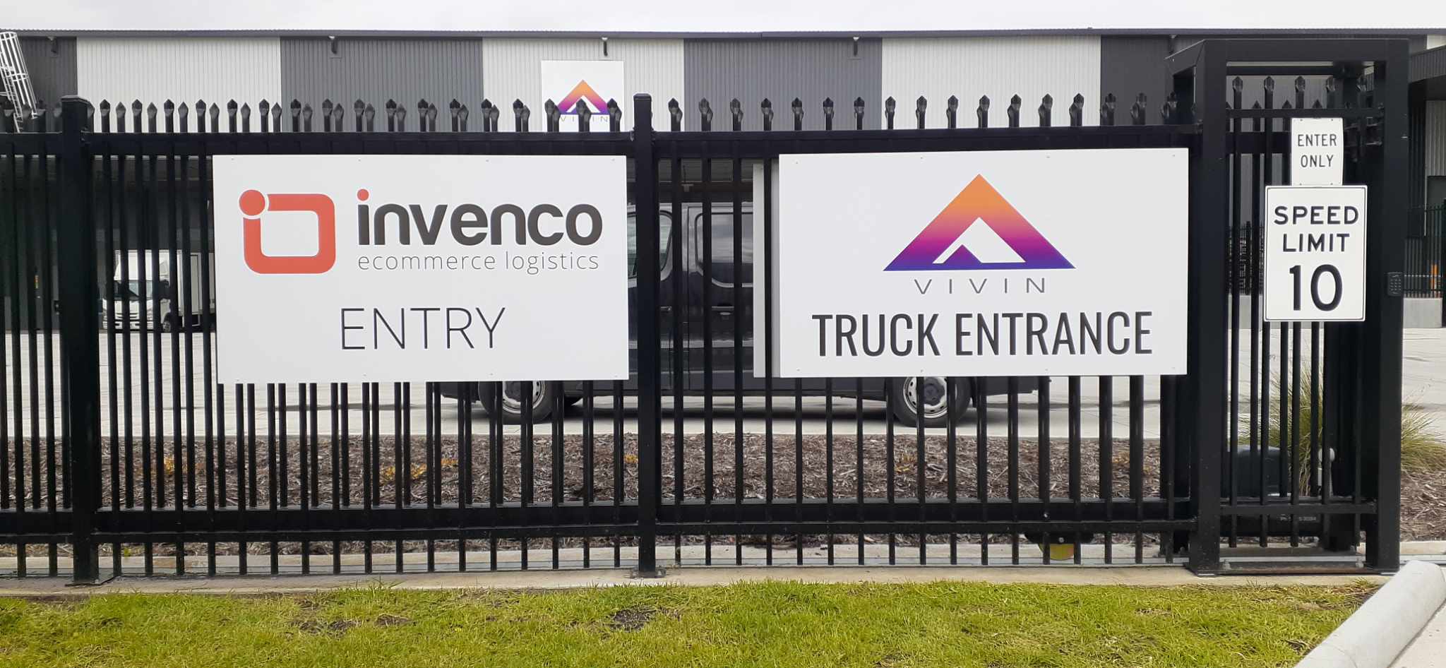 Fence with 'invenco' and 'Vivin' signs at an entrance. Both white aluminum composite panels and drilled into fencing