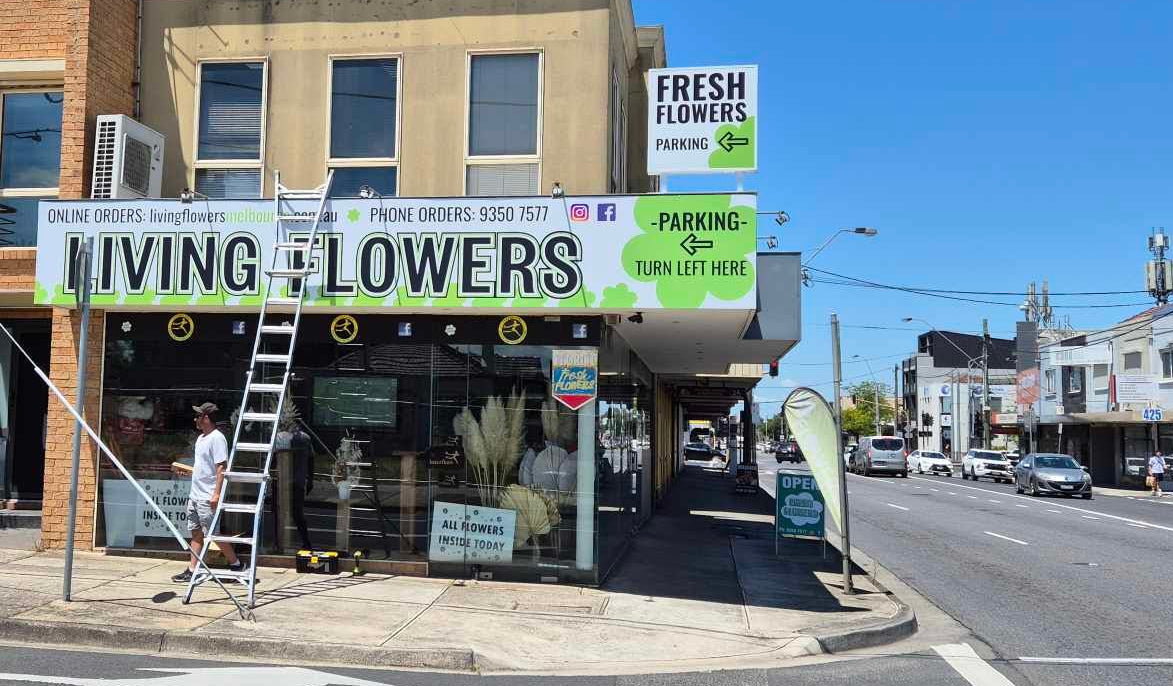 Street view of a building with a 'Living Flowers' sign on a clear day.