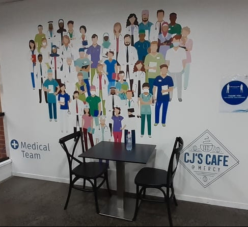 Café interior with wall mural of medical professionals and 'CJS Cafe' sign.