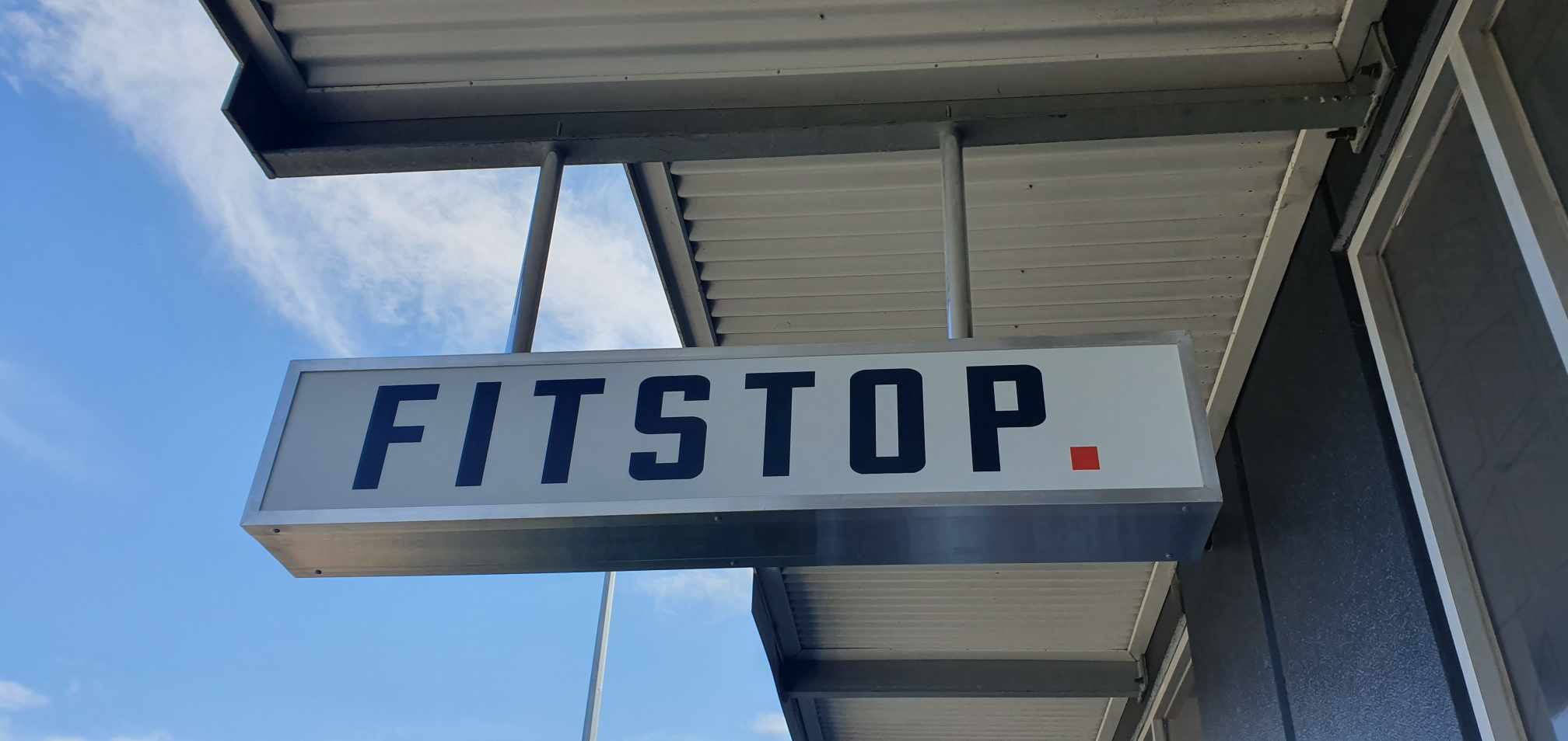 FITSTOP sign on a building with a blue sky background. Lights up at night and is good for under awning or roof